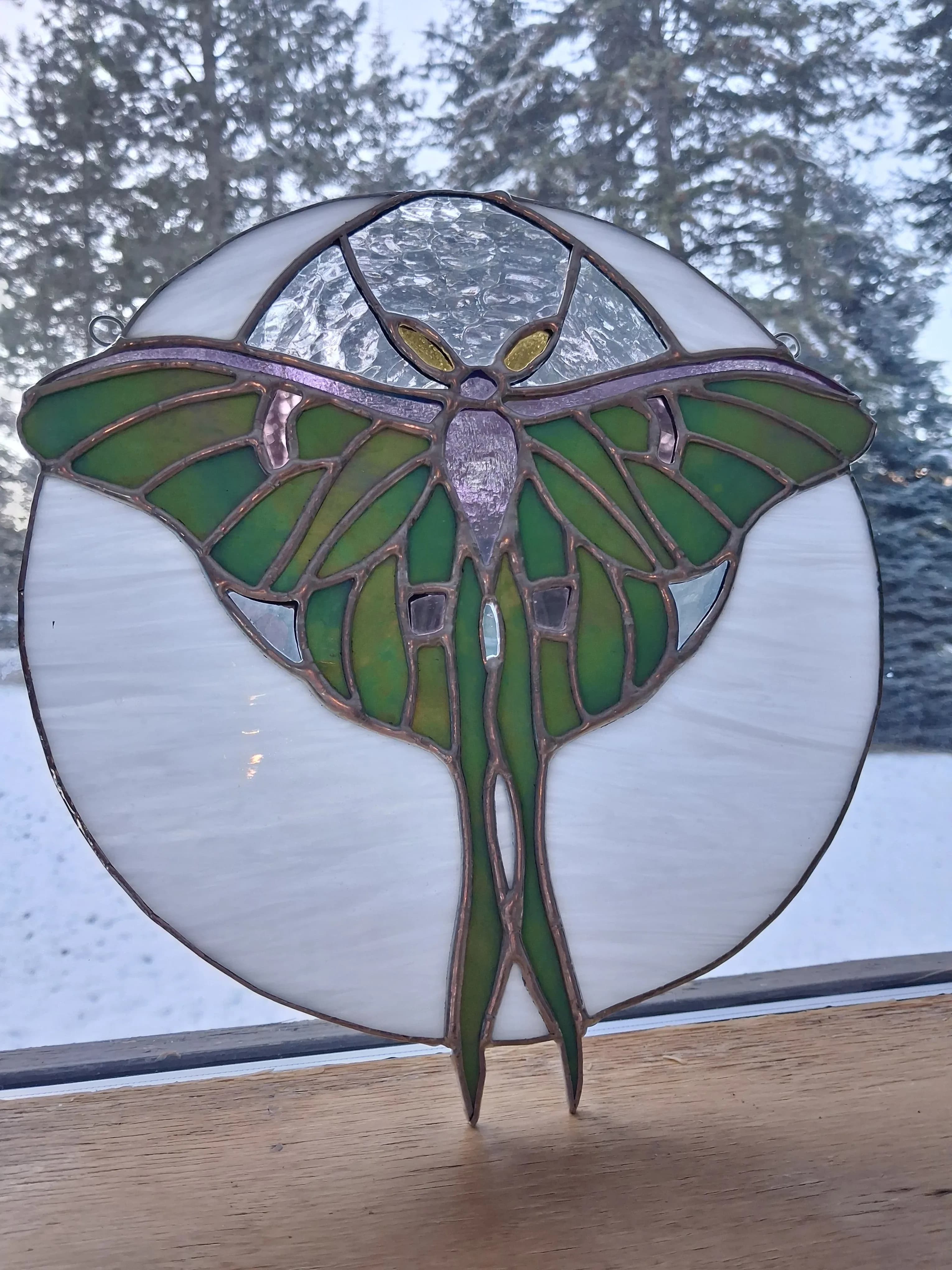 Green luna moth stained glass with copper foil detail on window with snowy landscape